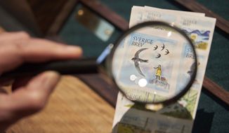 Swedish teenage environmental activist Greta Thunberg appears on a postal stamp in her native Sweden that is part of a series focusing on the environment, as seen through a magnifying glass, in Stockholm, Wednesday, Jan. 13, 2021. One of the stamps features teenage environmental activist Greta Thunberg in her trademark yellow raincoat with her braid blowing in the wind and standing a top a hill. (AP Photo/David Keyton)