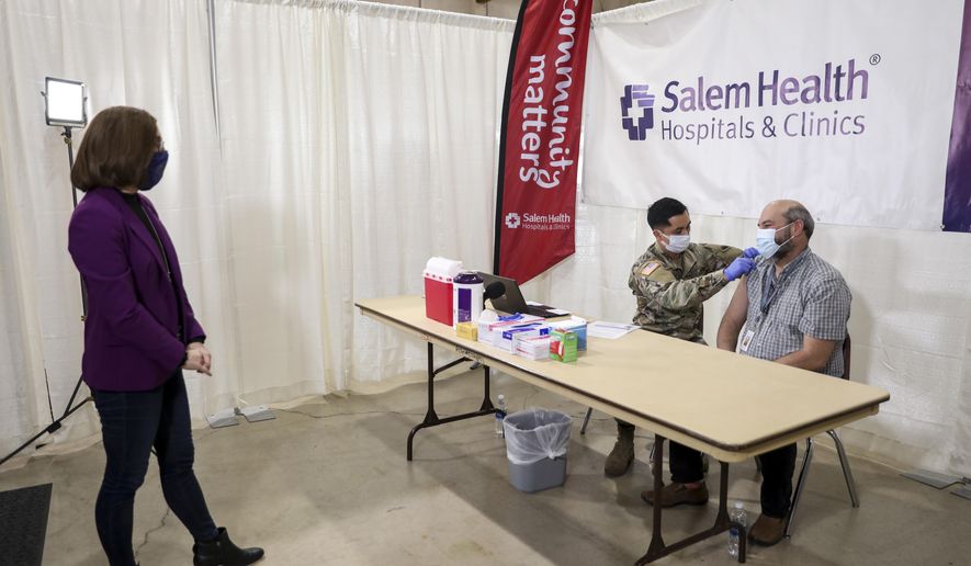 Oregon Gov. Kate Brown watches as a COVID-19 vaccine is administered by National Guard member Juan Carlos Rojas to Jason Mayberry at the Marion County and Salem Health vaccination clinic on Wednesday, Jan. 13, 2021, at the Oregon State Fairgrounds in Salem, Ore. (Abigail Dollins/Statesman-Journal via AP, Pool)