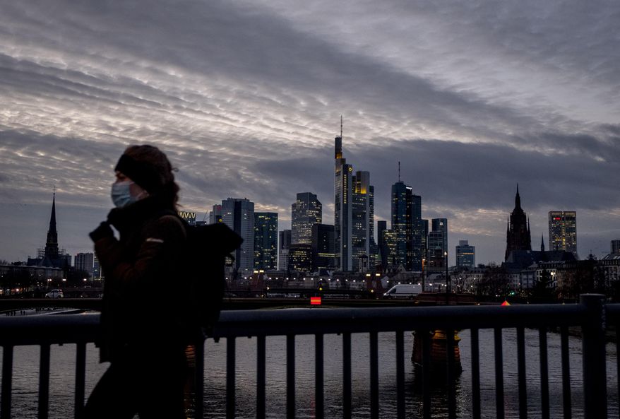 A woman wearing a face mask passes the skyline in Frankfurt, Germany, Wednesday, Jan. 13, 2021. (AP Photo/Michael Probst)