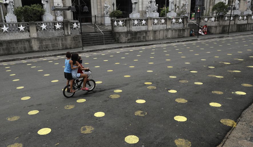 Children ride a bike past markers placed outside the Santo Nino Parish at Tondo district, Manila, Philippines on Friday, Jan. 15, 2021. The Manila city government said that the usual festivities are prohibited during the upcoming feast day of Santo Nino or Baby Jesus in Tondo and Pandacan to curb the spread of COVID-19 infections. Masses will be held at the church under strict health protocols this weekend. (AP Photo/Aaron Favila)