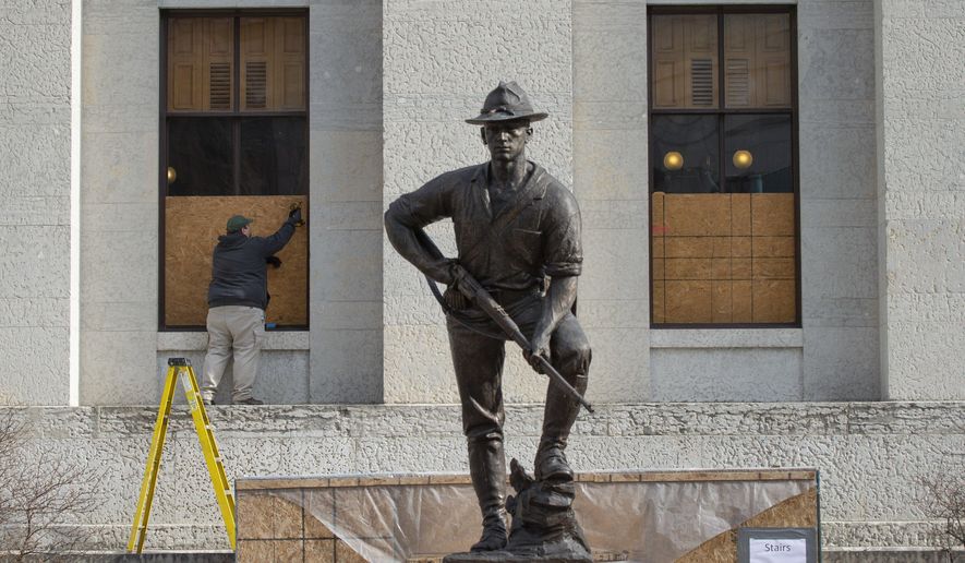Ohio Statehouse maintenance employees board up the windows of the building behind the United Spanish War Veterans Memorial statue in preparation for planned weekend protests in Columbus, Ohio, on Thursday, Jan. 14, 2021. The Statehouse and all state buildings in downtown Columbus will be closed Sunday through Wednesday. (Adam Cairns/The Columbus Dispatch via AP)