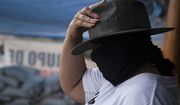 A masked woman who said she was displaced from her community by criminal groups adjusts her hat as she helps patrol a checkpoint run by a group of armed women who call themselves a self-defense group, at the entrance to El Terrero in Michoacan state, Mexico, Wednesday, Jan. 13, 2021. The rural area is traversed by dirt roads, through which they fear Jalisco gunmen could penetrate at a time when the homicide rate in Michoacán has spiked to levels not seen since 2013. (AP Photo/Armando Solis)