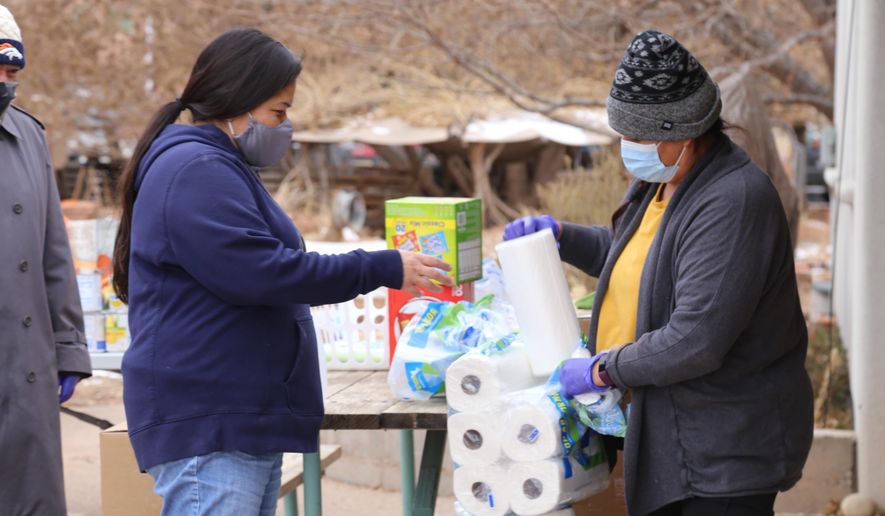 Miyoshi Lee, left, and Leslie Goldtooth, right, aid residents with some basic relief goods at the Full Circle Intertribal Center in Moab, Utah on Dec. 17, 2020. They said joining the group has helped them find a sense of community, where they've both lived for over two decades. The Utah-based nonprofit was founded to help build community among the Native population in Moab and has recently turned its attention to caring for Native elders during the coronavirus pandemic. (Kate Groetzinger/KUER, via AP)