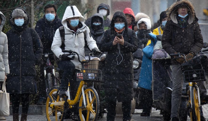 Commuters wearing face masks to protect against the spread of the coronavirus wait at an intersection during a snowy morning in Beijing, Tuesday, Jan. 19, 2021. A Chinese province near Beijing grappling with a spike in coronavirus cases is reinstating tight restrictions on weddings, funerals and other family gatherings, threatening violators with criminal charges. (AP Photo/Mark Schiefelbein)