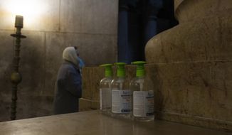 A woman attends mass next to three bottles of hand sanitizer available for worshippers at the Church of the Holy Sepulchre, where Jesus Christ is believed to be buried, during a third lockdown to curb the spread of the coronavirus, in the Old City of Jerusalem, Monday, Jan. 18, 2021. (AP Photo/Maya Alleruzzo)