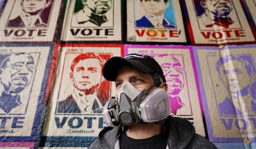 Artist Brandon Litman looks on as posters of U.S. Senator-elect's Jon Ossoff, D-Ga., and Raphael Warnock tower behind him after Georgia's Senate runoff race on Sunday, Jan. 10, 2021, in Atlanta. (AP Photo/Brynn Anderson)