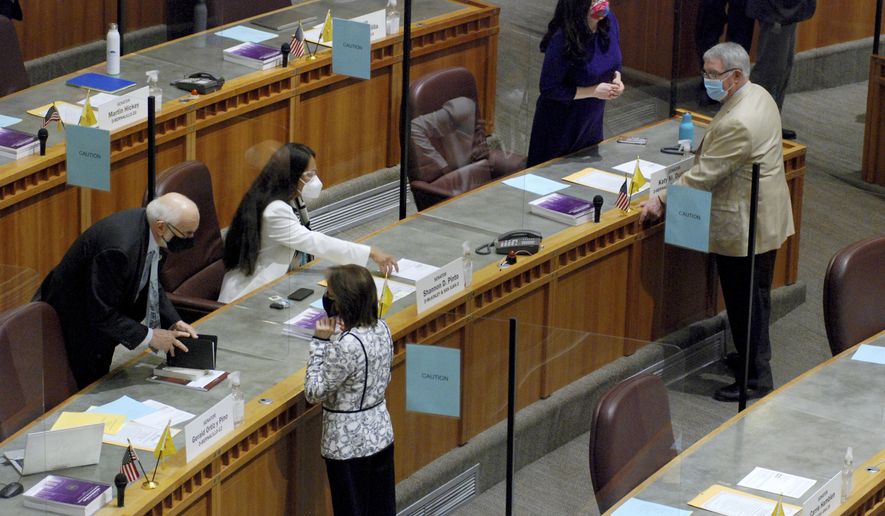 New Mexico state senators including Democratic Sens. Jerry Ortiz y Pino and Mimi Stewart, bottom left, both of Albuquerque, greet each other on Tuesday, Jan. 19, 2021, in Santa Fe, N.M., on the first day of a 60-day legislative session. Fences, roadblocks, police and troops encircled the building as a precaution against federal warnings about the potential for violence. Plexiglass partitions have been installed on the floor of the House and Senate to protect legislators from coronavirus infection, and the Capitol is closed to the public to blunt the contagion. (AP Photo/Morgan Lee)