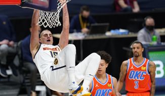 Denver Nuggets center Nikola Jokic, left, hangs from the rim after dunking the ball for a basket against Oklahoma City Thunder forward Isaiah Roby, center, and guard George Hill in the first half of an NBA basketball game Tuesday, Jan. 19, 2021, in Denver. (AP Photo/David Zalubowski)
