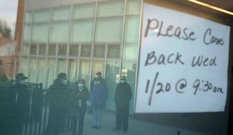 People waiting in line are reflected in the glass windows of a vaccination site in Paterson, N.J., Tuesday, Jan. 19, 2021. A sign on the door of the vaccination site, which takes walk-ins rather than appointments, said it would be open the following day on Wednesday. (AP Photo/Seth Wenig)