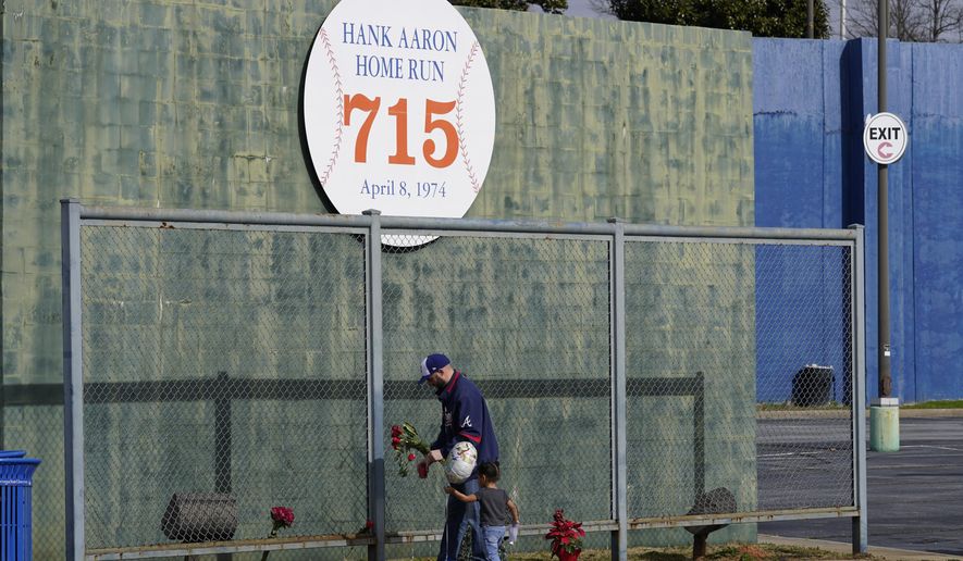 Les Motes and his two-year-old daughter Mahalia leave flowers, Friday, Jan. 22, 2021, in Atlanta, near the spot where a ball hit for a home run by Atlanta Braves&#x27; Hank Aaron cleared the wall to break Babe Ruth&#x27;s career home run record in 1974. Aaron, who endured racist threats with stoic dignity during his pursuit of Babe Ruth but went on to break the career home run record in the pre-steroids era, died peacefully in his sleep early Friday. He was 86. (AP Photo/John Bazemore)