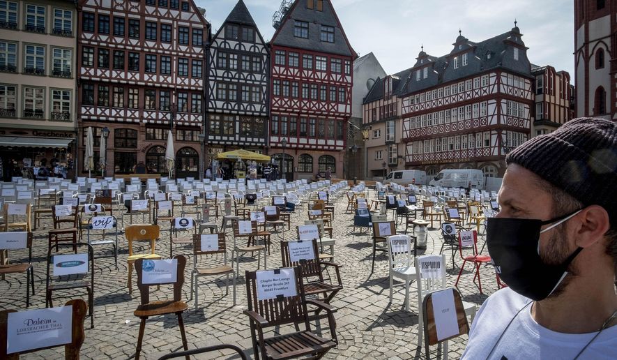 In this April 24, 2020, file photo, a man with a face mask watches empty chairs with names of bars and restaurants on the Roemerberg square in Frankfurt, Germany. More than 50,000 people have died after contracting COVID-19 in Germany, a number that has risen swiftly over recent weeks as the country has struggled to bring down infection figures. (AP Photo/Michael Probst, File)