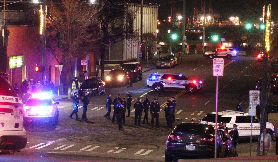 Tacoma Police and other law enforcement officers stand in an intersection near the site of a car crash Saturday, Jan. 23, 2021, in downtown Tacoma, Wash. At least one person was injured when a police car plowed through a crowd of people Saturday night who were watching a downtown street race, the Tacoma News-Tribune reported. (AP Photo/Ted S. Warren)