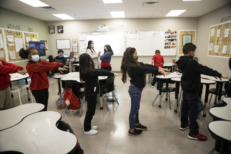 Students reach out with their arms to practice social distancing while walking to their next class at Mater Academy East Campus in Las Vegas, Wednesday, Jan. 13, 2021. Students who attend the school clean their desks at the end of the day and walk through halls and rooms with COVID-19 air purifiers to kill viruses in the air. (Erik Verduzco/Las Vegas Review-Journal via AP)