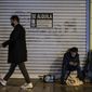 A homeless with his little pet, bottom right, in front a store to rent for food, begs for alms while pedestrian walking past wearing face mask protection against the coronavirus, in Pamplona, northern Spain, Thursday, Jan. 21, 2021. (AP Photo/Alvaro Barrientos)