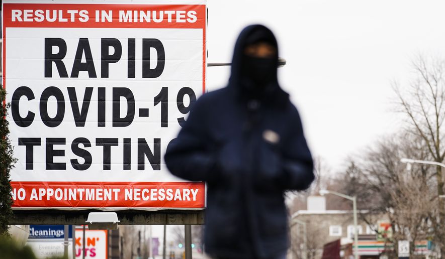 A person wearing face mask as a precaution against the coronavirus walks near a sign advertising a rapid COVID-19 testing site in Philadelphia, Monday, Jan. 25, 2021. (AP Photo/Matt Rourke)