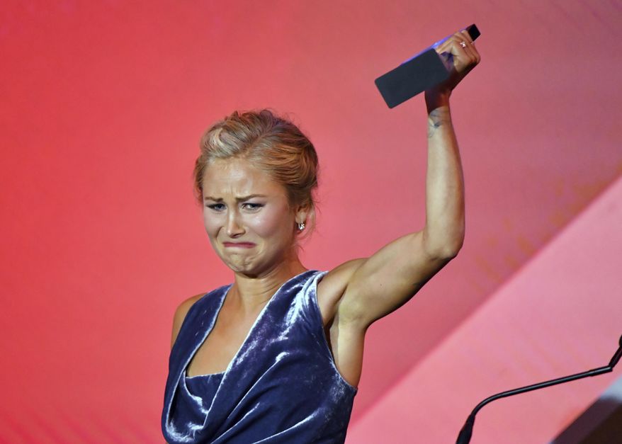 Australian of the Year winner Grace Tame raises her award during a ceremony in Canberra, Monday, Jan. 25, 2021. Tame, 26, pushed for legal changes so she could speak out about being a survivor of the sexual abuse she went through as a 15-year-old at the hands of a math teacher. (Mick Tsikas/AAP Image via AP)