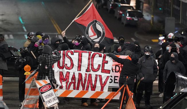 In this file photo, a protester carries a flag that reads &#x27;Antifascist Action&#x27; near a banner that reads &#x27;ustice for Manny,&#x27; during a protest against police brutality, late Sunday, Jan. 24, 2021, in downtown Tacoma, Wash., south of Seattle. (AP Photo/Ted S. Warren) **FILE**