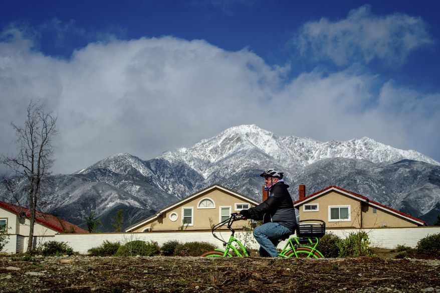 A cyclist rides a bike along the Pacific Electric Trail in Rancho Cucamonga, Calif. against a backdrop of the snow-capped San Gabriel Mountains on Monday, Jan. 25, 2021. (Watchara Phomicinda/The Orange County Register via AP)