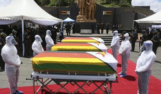 Pallbearers stand next to coffins of three top government officials at their burial at the National Heroes acre in Harare, Wednesday, Jan, 27, 2021. Zimbabwe on Wednesday buried three top officials who succumbed to COVID-19, in a single ceremony at a shrine reserved almost exclusively for the ruling elite as a virulent second wave of the coronavirus takes a devastating toll on the country.( AP Photo/Tsvangirayi Mukwazhi)