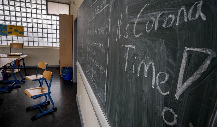 FILE - In this Friday, March 13, 2020 file photo the slogan 'It's Corona Time' is written on the chalkboard of an empty classroom of a high school in Frankfurt, Germany. The German government on Wednesday agreed on a strategy to boost the use of data for commercial purposes and signed a deal with state education authorities to fund laptops for teachers who have to work from home because of the virus lockdown. (AP Photo/Michael Probst, file)