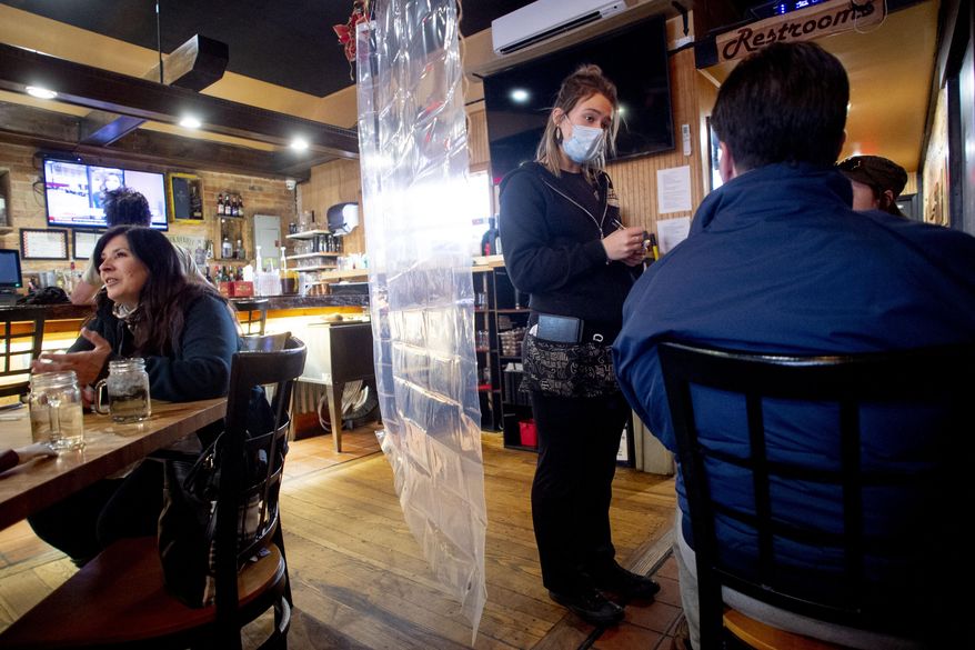 FILE - In this Nov. 24, 2020, file photo, Waitress Rikkie Schleben takes down lunch orders from Tabitha Kemble, right, and her father Ken Kemble for dine-in service at Woodchips BBQ in Lapeer, Mich. Several states are loosening their coronavirus restrictions on restaurants and other businesses because of improved infection and hospitalization numbers but are moving cautiously, in part because of the more contagious variant taking hold in the U.S. (Jake May/The Flint Journal via AP, File)