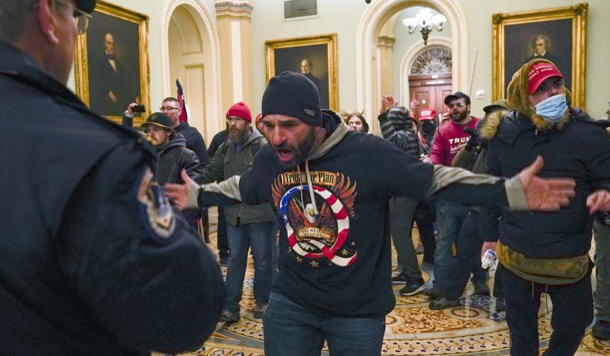 In this Wednesday, Jan. 6, 2021 file photo, Trump supporters, including Doug Jensen, center, confront U.S. Capitol Police in the hallway outside of the Senate chamber at the Capitol in Washington. QAnon conspiracy theory believers were front and center at the Jan. 6 rally in support of Trump’s baseless claims of widespread election fraud as well as the riot that followed. (AP Photo/Manuel Balce Ceneta)