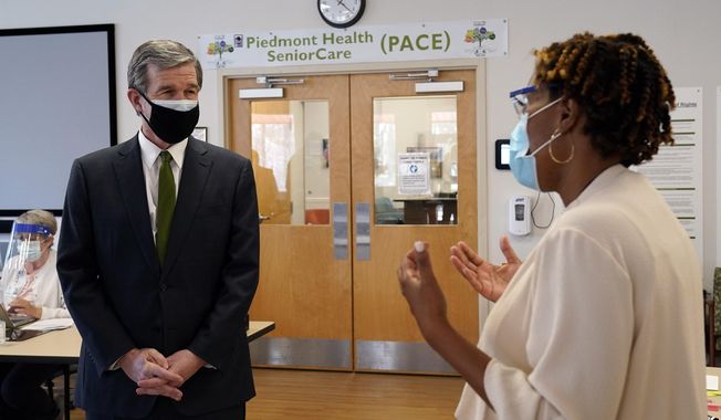 Gov. Roy Cooper, left, speaks with Misty Drake, Chief Operating Officer at Piedmont Health Senior Care, a federally qualified health center where PACE patients (Program of All-Inclusive Care for the Elderly) and underserved populations can receive the COVID-19 vaccine Thursday, Jan. 28, 2021 in Pittsboro, N.C. (AP Photo/Gerry Broome)