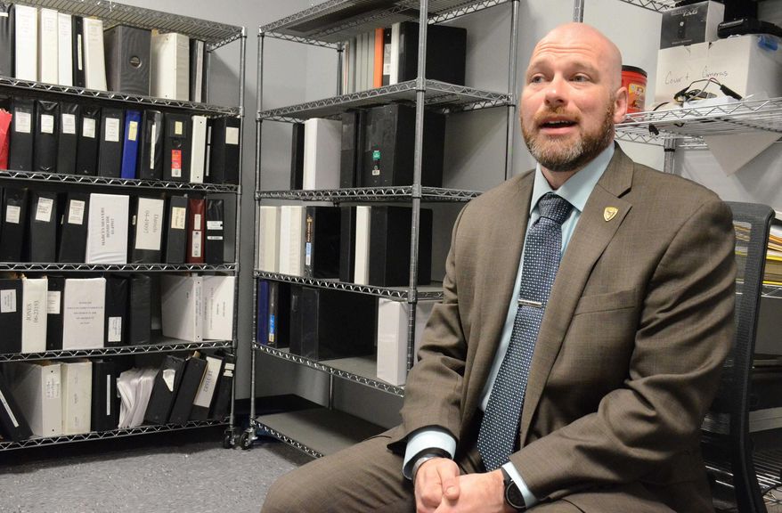 Detective Scott Marshall poses with some of the cold case files at the Battle Creek Creek Police Department on Nov. 3, 2019, in Battle Creek, Mich. Police said they solved the murder of a Battle Creek woman more than 30 years later, after a newly discovered blood sample connected a man to the fatal stabbing. But no charges will be filed because Roger Plato was killed in 1988, three days before Gayle Barrus' body was found by hunters in Calhoun County, prosecutor David Gilbert said. (Trace Christenson/Battle Creek Enquirer via AP)