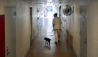 FILE - This photo from Monday June 21, 2004, shows New Jersey&#39;s Edna Mahan Correctional Facility inmate Mary Tobin, walking a puppy down a cell block hallway as part of a program called Puppies Behind Bars, where dogs are cared for until they are ready to be expertly trained to detect explosives or as guide dogs for the blind. Dozens of corrections officers at New Jersey&#39;s only women&#39;s prison have been placed on paid leave following allegations that staff brutally beat and sexually assaulted inmates there. (AP Photo/Daniel Hulshizer, File)