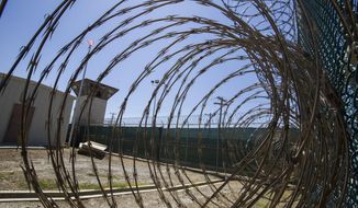FILE - In this Wednesday, April 17, 2019 file photo reviewed by U.S. military officials, the control tower is seen through the razor wire inside the Camp VI detention facility in Guantanamo Bay Naval Base, Cuba.  The U.S. is backing off for now on a plan to offer COVID-19 vaccinations to the 40 prisoners held at the detention center at Guantanamo Bay, Cuba.Pentagon chief spokesman John Kirby said in a tweet Saturday, Jan. 30, 2021 that the Defense Department would be “pausing” the plan to give the vaccination to those held at Guantanamo while it reviews measures to protect troops who work there. (AP Photo/Alex Brandon, File)