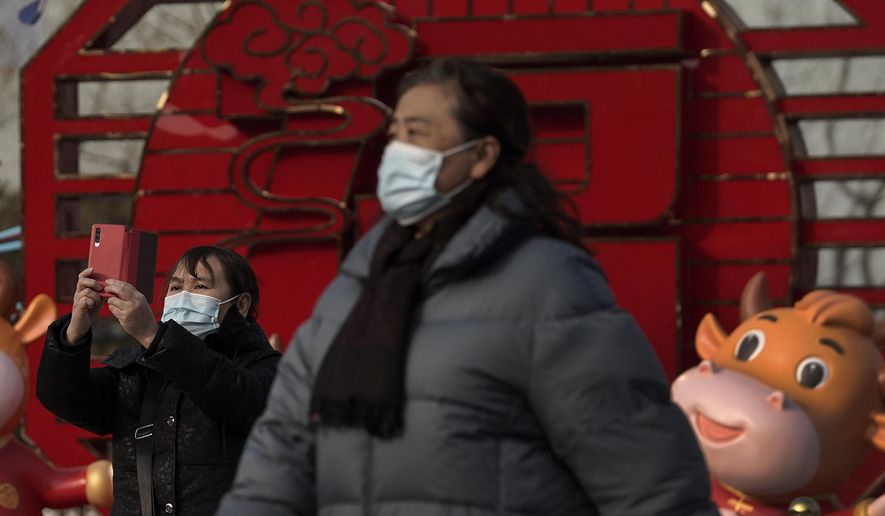 A woman wearing a face mask to help curb the spread of the coronavirus takes a souvenir photo near a Lunar New Year decoration with ox figures at Qianmen Street, a popular tourist spot in Beijing, Sunday, Jan. 31, 2021. A World Health Organization team looking into the origins of the coronavirus pandemic on Sunday visited the seafood market in the Chinese city of Wuhan that was linked to many early infections. (AP Photo/Andy Wong)