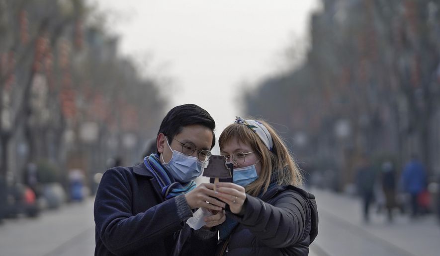 Visitors wearing face masks to help curb the spread of the coronavirus take a smartphone photo of an ice-cream with a shaped of Qianmen Gate which bought at Qianmen Street, a popular tourist spot in Beijing, Sunday, Jan. 31, 2021. A World Health Organization team looking into the origins of the coronavirus pandemic on Sunday visited the seafood market in the Chinese city of Wuhan that was linked to many early infections. (AP Photo/Andy Wong)