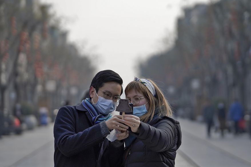 Visitors wearing face masks to help curb the spread of the coronavirus take a smartphone photo of an ice-cream with a shaped of Qianmen Gate which bought at Qianmen Street, a popular tourist spot in Beijing, Sunday, Jan. 31, 2021. A World Health Organization team looking into the origins of the coronavirus pandemic on Sunday visited the seafood market in the Chinese city of Wuhan that was linked to many early infections. (AP Photo/Andy Wong)