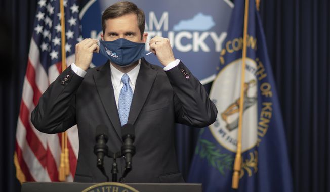 Kentucky Gov. Andy Beshear takes off his facial mask before providing an update on the COVID-19 pandemic in the state during a media conference at the Kentucky state Capitol in Frankfort, Ky., on Thursday, Jan. 21, 2021. (Ryan C. Hermens/Lexington Herald-Leader via AP)