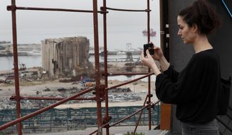 Joana Dagher, 33, who lost her memory for two full months from the trauma she suffered in the massive August explosion at the Beirut port, including a cerebral contusion and brain lesions, takes pictures of the explosion scene from her damaged apartment rooftop, in Beirut, Lebanon, Wednesday, Jan. 27, 2021. The mental health impact of the Beirut explosion that killed more than 200 and wounded more than 6,000 continues to lay its heavy weight on those who managed to survive the day. (AP Photo/Hussein Malla)