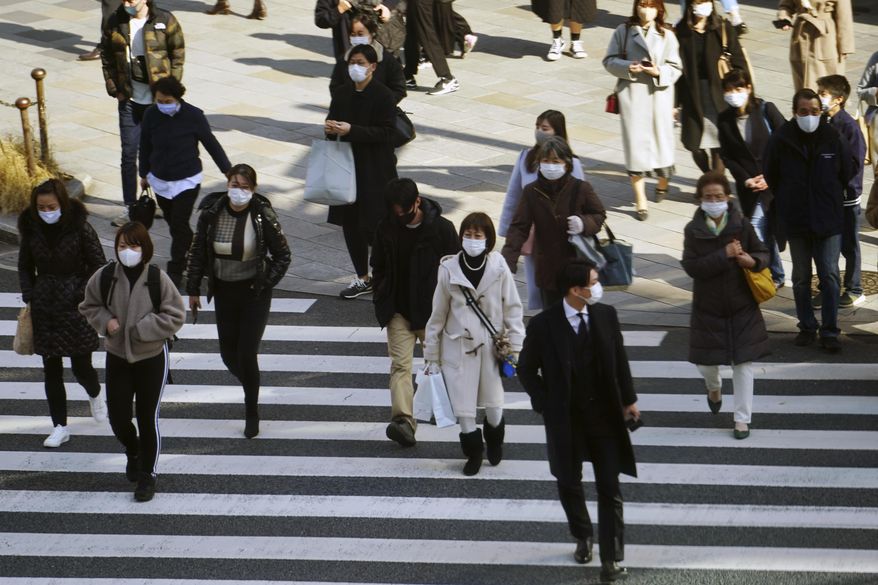 People wearing protective masks to help curb the spread of the coronavirus walk along a pedestrian crossing Monday, Feb. 1, 2021, in Tokyo. The Japanese capital confirmed more than 390 new coronavirus cases on Monday. (AP Photo/Eugene Hoshiko)