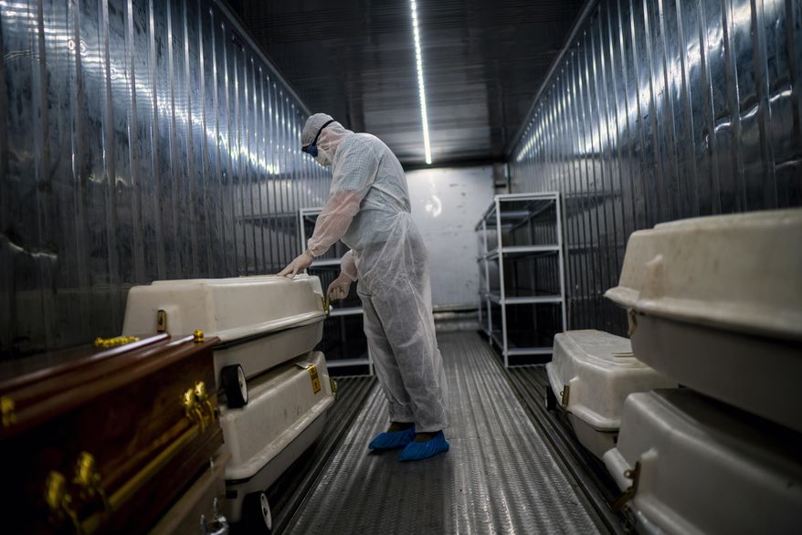 An AVBOB mortuary employee wearing full PPE checks coffins containing the remains of COVID-19 victims in a refrigerated container in Johannesburg, Tuesday, Feb. 2, 2021, one day after South Africa gave a hero's welcome to the delivery of its first COVID-19 vaccines — 1 million doses of the AstraZeneca vaccine produced by the Serum Institute of India. (AP Photo/Jerome Delay)