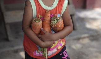 A child carries an armful of donated carrots to her mother who is helping prepare lunch at a soup kitchen in the Villa Maria shantytown of Lima, Peru, Tuesday, Feb. 2, 2021, amid a second complete lockdown in less than a year as Peru battles a resurgence in COVID-19 cases. The lack of a steady income has forced many families to become dependent of community soup kitchens in some of the capital’s poorest neighborhoods. (AP Photo/Martin Mejia)