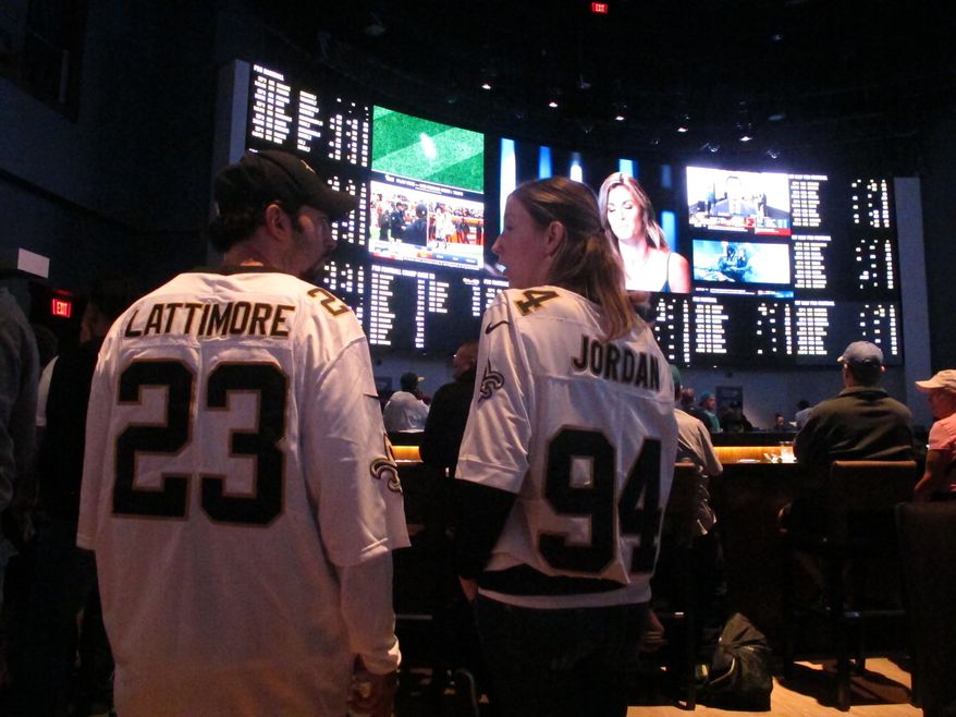 FILE: This Sept. 9, 2018 file photo shows football fans waiting for kickoff in the sports betting lounge at the Ocean Casino Resort in Atlantic City, N.J. A report released Feb. 2, 2021 by the American Gaming Association predicts fewer Americans will bet on this year's Super Bowl, a decrease driven largely by fewer people back at work in offices where betting pools are circulated. But the report also predicts a record amount will be wagered online this year. (AP Photo/Wayne Parry, FILE)