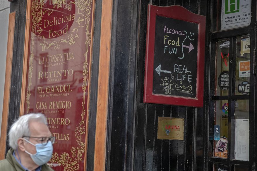 A man wearing a protective mask walks by El Cano pub with a sign to encourage people to visit the pub and terrace in Madrid, Spain, Tuesday, Feb. 2, 2021. Spain's virus expert for the coronavirus pandemic says infections in the country are losing steam but that the contagion curve needs to be bent much further to safeguard the health system. (AP Photo/Paul White)