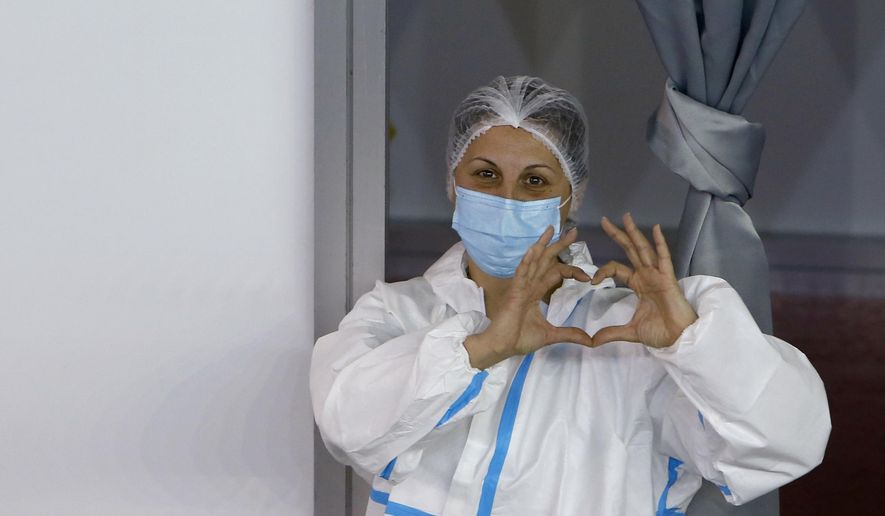 A medical worker wearing protective gear gestures as people wait to receive the COVID-19 vaccine, at Belgrade Fair makeshift vaccination center, in Belgrade, Serbia, Monday, Jan. 25, 2021. Serbia were the first European country to receive the Chinese Sinopharm&#39;s vaccine for mass inoculation programmes. (AP Photo/Darko Vojinovic)