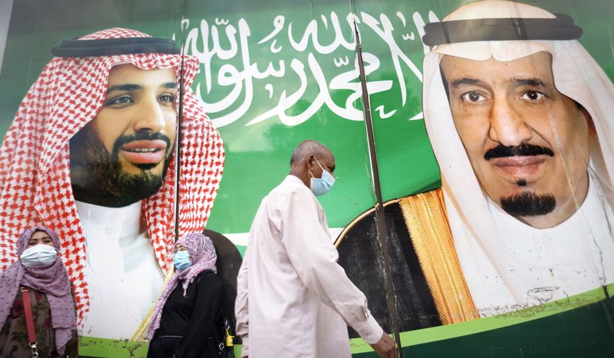 People wear face masks to protect against the spread of the coronavirus in front of a banner showing Saudi King Salman, right, and his Crown Prince Mohammed bin Salman, outside a mall in Jiddah, Saudi Arabia, Friday, Feb. 5, 2021. In Saudi Arabia, where authorities already have banned travel to the kingdom from 20 countries including the U.S., officials ordered all weddings and parties suspended. It closed down all shopping malls, gyms and other locations for 10 days, as well as indoor dining. (AP Photo/Amr Nabil)