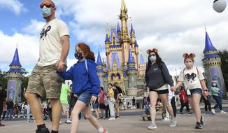 A masked family walks past Cinderella Castle in the Magic Kingdom, at Walt Disney World in Lake Buena Vista, Fla., Monday, Dec. 21, 2020. Disney&#39;s Florida parks are currently operating at 35% capacity due to the Covid-19 pandemic. (Joe Burbank/Orlando Sentinel via AP)