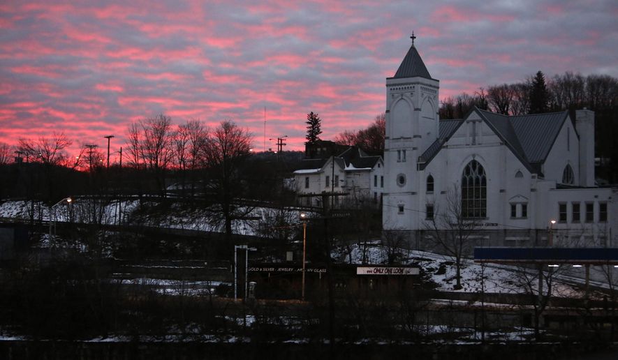 The sky lights up at dawn behind First Presbyterian Church and the rail yard in the historic coal city of Bluefield, W.Va, on Saturday, Jan. 24, 2021.  Members of three congregations in a small city in West Virginia’s ‘Trump Country’ face a reckoning over Christianity and the misuse of symbols of their faith in America’s divisive politics.  (AP Photo/Jessie Wardarski)