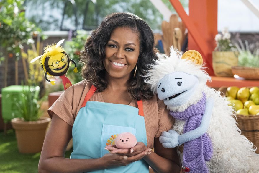 This image released by Netflix shows former first lady Michelle Obama with Busy, a bee puppet, left, Mochi, a pink round puppet, and Waffles, a furry puppet with waffle ears on the set of the children&#39;s series &amp;quot;Waffles + Mochi.&amp;quot;  Obama is launching the new Netflix children’s food show on March 16. (Adam Rose/Netflix via AP)