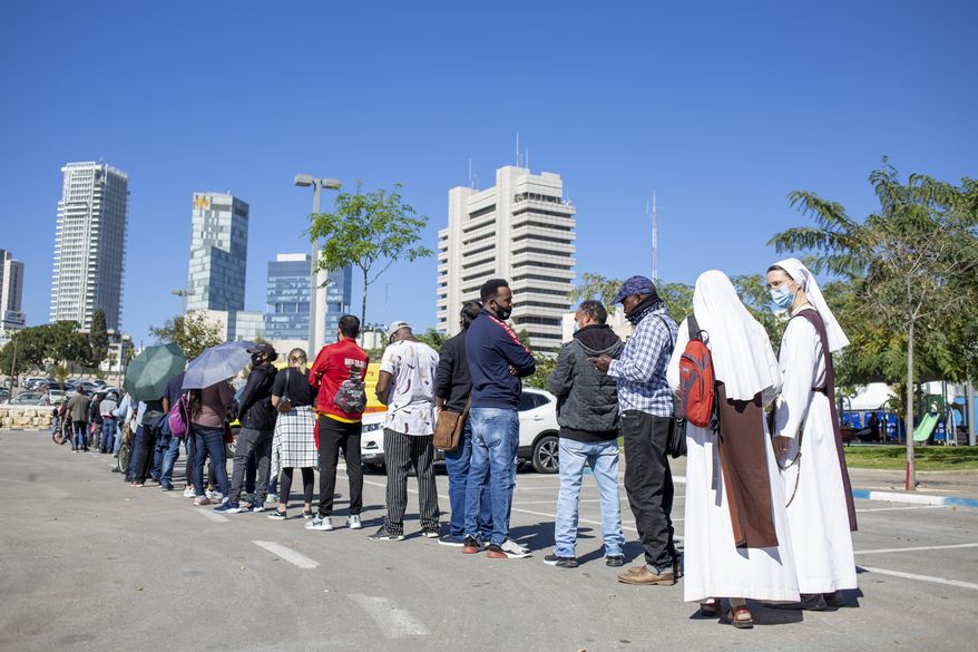 Nuns, asylum seekers and foreign workers wait in line to receive their first dose of the Pfizer-BioNTech coronavirus vaccine at a vaccination center in Tel Aviv, Israel, Tuesday, Feb. 9, 2021. Tel Aviv City Hall and the Sourasky Medical Center started administering vaccines free of charge to the city's foreign nationals, many of whom are undocumented asylum seekers. (AP Photo/Ariel Schalit)