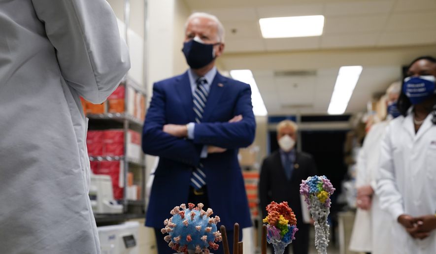 With a model of the COVID-19 virus displayed, President Biden listens as Dr. Barney Graham, left, speaks during a visit at the Viral Pathogenesis Laboratory at the National Institutes of Health (NIH), Thursday, Feb. 11, 2021, in Bethesda, Md. Kizzmekia Corbett, an immunologist with the Vaccine Research Center at the NIH, listens at right. (AP Photo/Evan Vucci)