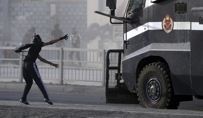 File - In this Friday, March 15, 2013 file photo, a Bahraini anti-government protester throws a piece of wood at an armored police vehicle during clashes in Jidhafs, Bahrain. A decade ago, against all odds, a popular uprising convulsed the monarchy of Bahrain as a wave of revolutionary protests swept across the Middle East. But after a brutal crackdown and years of escalating repression, activists say the small kingdom is less free now than even before the Arab Spring, as authorities crush hopes for political reform. (AP Photo/Hasan Jamali, File)