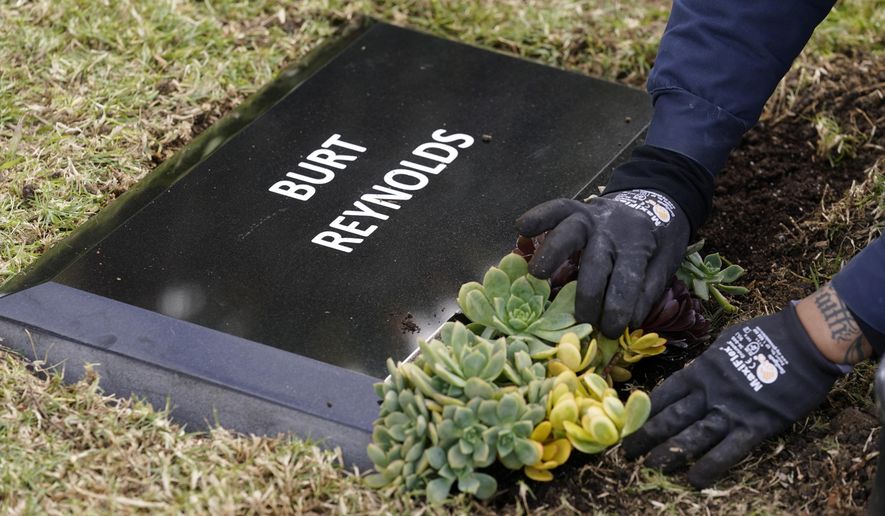 Flowers are placed in front of a temporary headstone for the late actor Burt Reynolds in the Garden of Legends section of Hollywood Forever cemetery, Thursday, Feb. 11, 2021, in Los Angeles. Reynolds' cremated remains were moved from Florida to Hollywood Forever, where a small ceremony was held Thursday. A permanent gravesite will be put up for Reynolds in a few months. (AP Photo/Chris Pizzello)