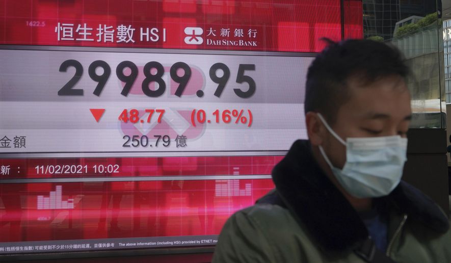 A man wearing a face mask walks past a bank's electronic board showing the Hong Kong share index in Hong Kong, Thursday, Feb. 11, 2021. Despite a short drop in early trading in Hong Kong, most major Asian stock indexes were higher on Thursday after President Joe Biden held his first conversation with Chinese leader Xi Jinping since taking office. (AP Photo/Kin Cheung)